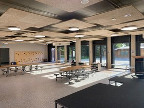 Ein großer heller Raum mit einer Tribüne im Vordergrund, zwei Tischen und einer Kletterwand im Hintergrund.