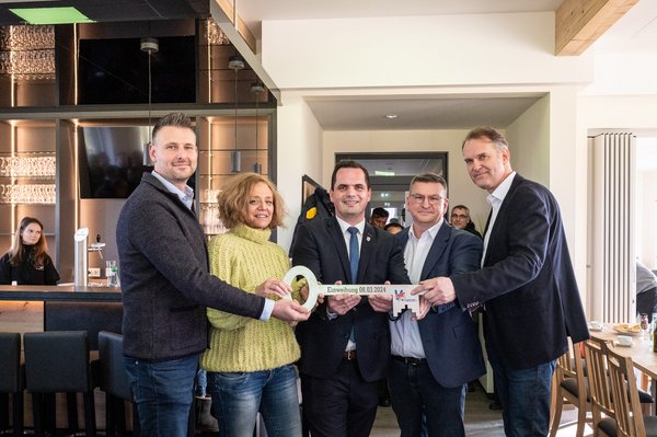 Die in der Bildbeschreibung genannten Personen halten gemeinsam einen großen Schlüssel in den Händen.