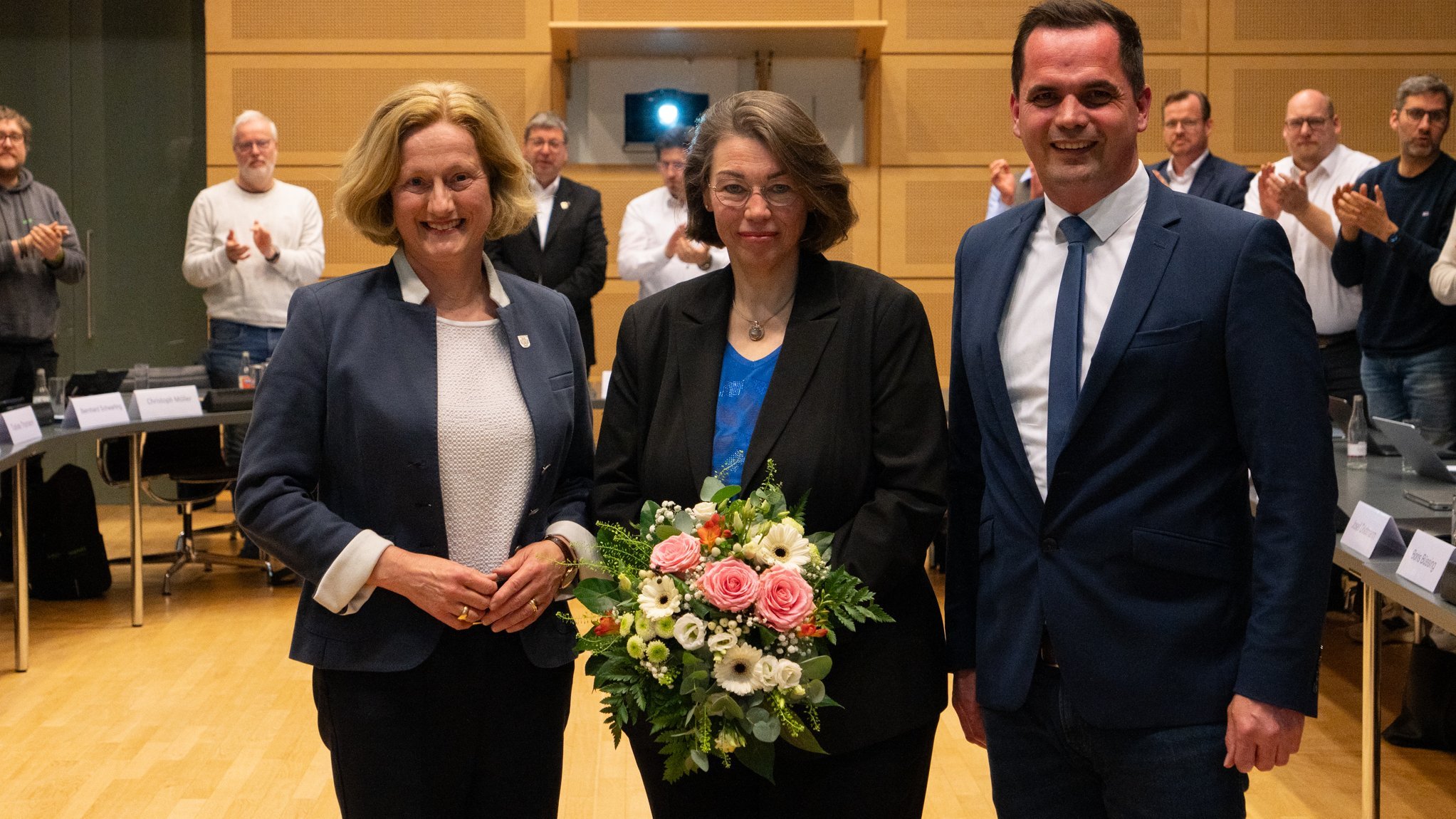 Die in der Bildunterschrift genannten Personen stehen im Zentrum des Ratsaals im Rathaus Vechta. Sandra Sollmann hält einen Blumenstraß in Händen.