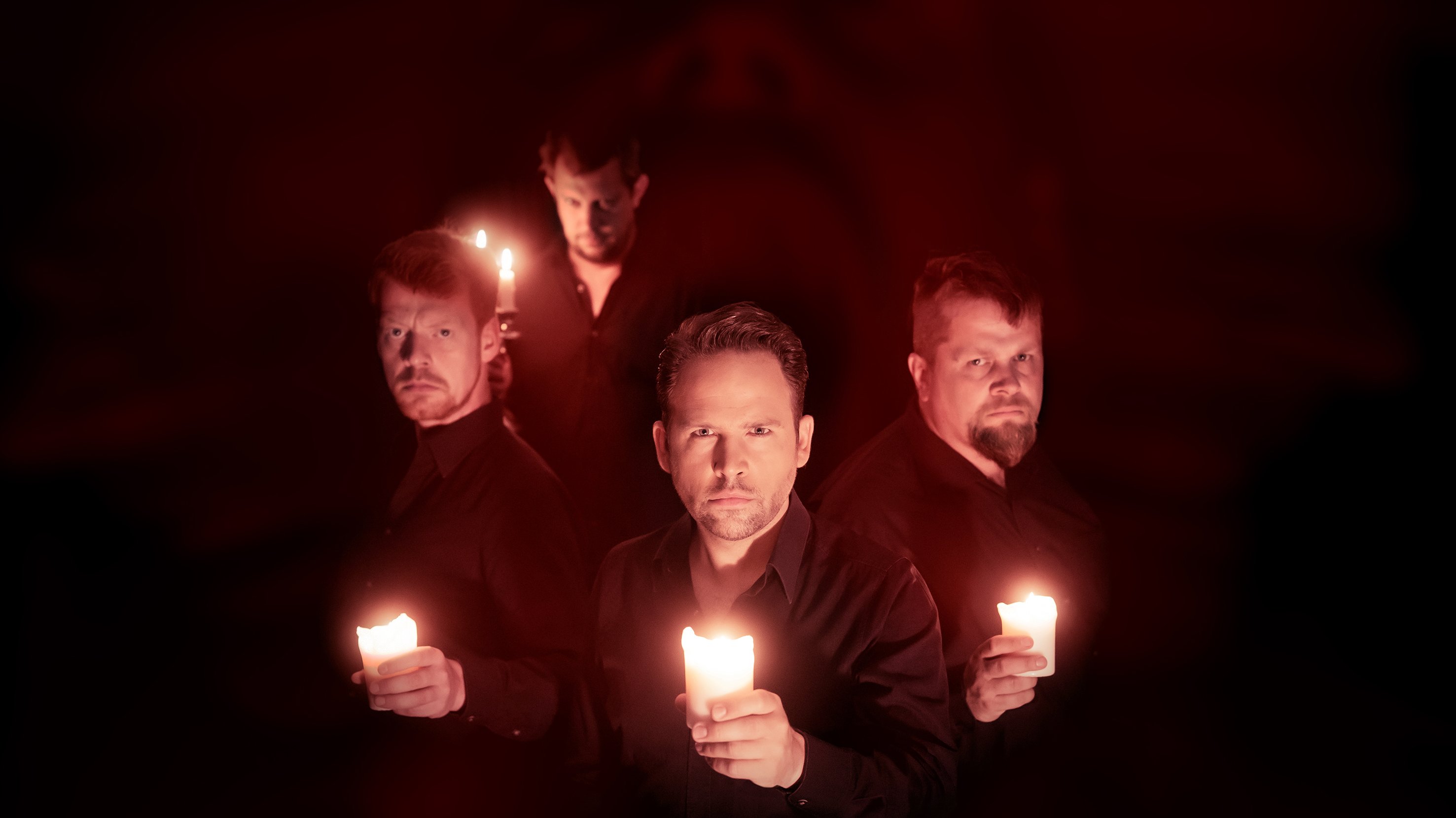 Vier Männer stehen mit Kerzen im Dunkeln