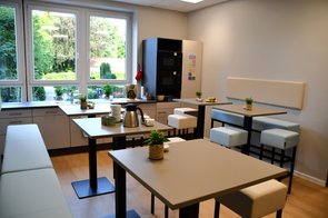 Der Küchenbereich mit mehreren Tischen, Kühlschrank und 2 Backöfen zeigt die Möglichkeiten für die Lehrkörper sich in der Mittagspause zu stärken.