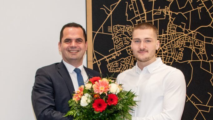 Bürgermeister Kristian Kater gratuliert Jason Bahns und übergibt einen Blumenstrauß.